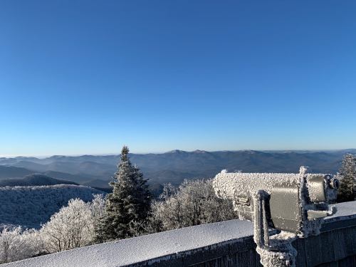 Snow-covered mountains under a clear blue sky, with a telescope overlooking the scenic view.
