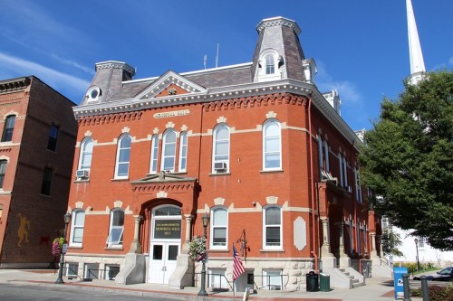 Historic red brick building with decorative architecture, featuring large windows and a flag in front against a blue sky.