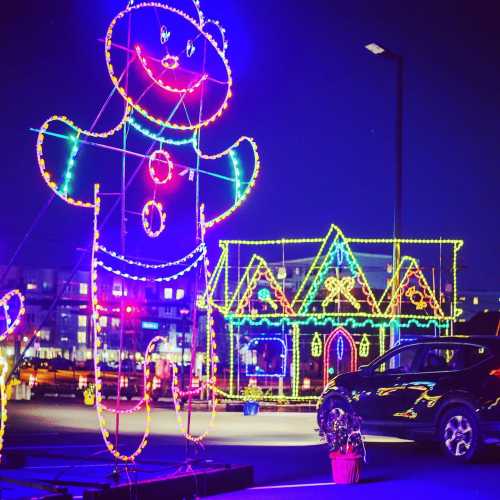 A large illuminated gingerbread man stands next to a brightly lit gingerbread house in a festive display at night.