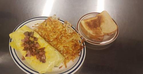 A plate with a cheese omelet topped with ham, crispy hash browns, and a side of toasted bread.