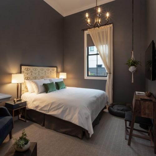 Cozy bedroom with a white bed, green pillows, a window, and stylish decor, featuring a chandelier and plants.