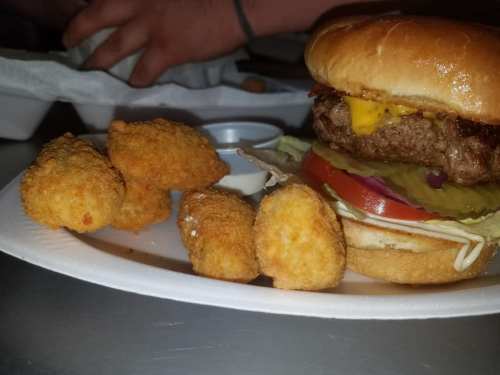 A close-up of a cheeseburger with lettuce, tomato, and pickles, accompanied by crispy chicken nuggets on a plate.