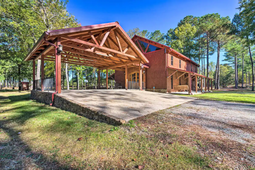 A spacious wooden structure with a covered patio, surrounded by trees and open grassland.