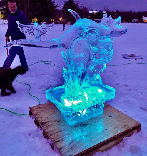 An illuminated ice sculpture of a kangaroo on a snowy landscape, with a person and a dog nearby.
