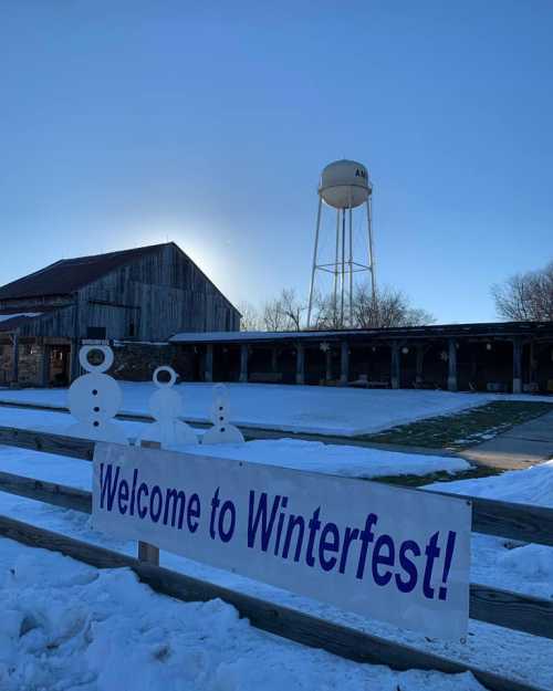 A snowy scene with a "Welcome to Winterfest!" sign, snowmen, a barn, and a water tower in the background.