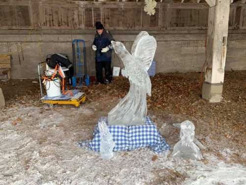 An ice sculptor works on a large eagle sculpture, with smaller ice figures nearby, in a snowy outdoor setting.