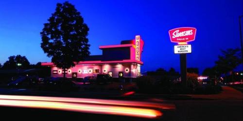 A diner at dusk with neon lights, featuring a sign that reads "Simpson's Drive-In" and a tree in the foreground.