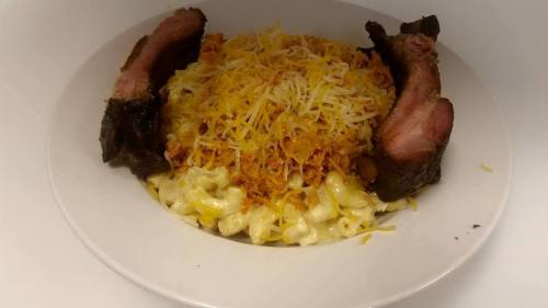 A plate of creamy macaroni and cheese topped with shredded cheese and two slices of smoked brisket on the sides.