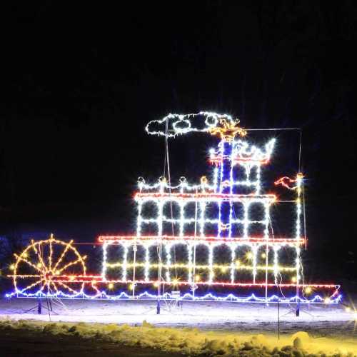 A brightly lit decorative display of a steamboat made of colorful lights against a dark night sky.