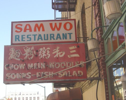 Sign for Sam Wo Restaurant featuring text in English and Chinese, advertising chow mein, noodles, soups, fish, and salad.
