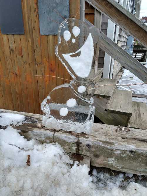 An ice sculpture of a cheerful snowman character sits on a snowy wooden surface.