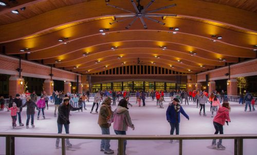 A lively indoor ice skating rink filled with skaters of all ages enjoying the activity under warm lighting.