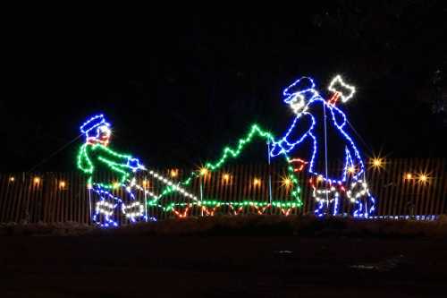 Two illuminated figures in blue and green, one holding an axe, appear to be cutting a Christmas tree.