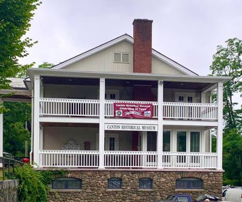 Front view of the Canton Historical Museum, featuring a two-story building with a banner and wraparound porch.