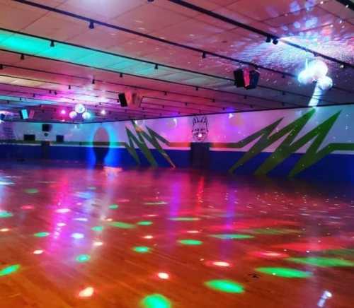 A brightly lit roller skating rink with colorful lights and a vibrant mural on the wall.