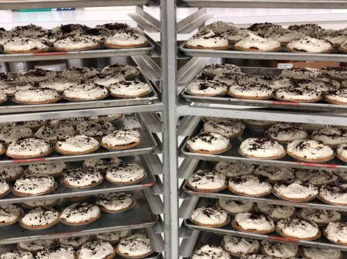 Trays of freshly baked cookies topped with cream and chocolate sprinkles, stacked in a bakery.