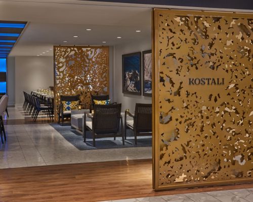 Entrance to a modern restaurant named "Kostali," featuring decorative gold screens and a stylish seating area.