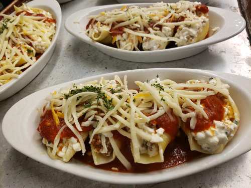 Three pasta dishes filled with cheese and meat, topped with marinara sauce and shredded cheese, garnished with parsley.
