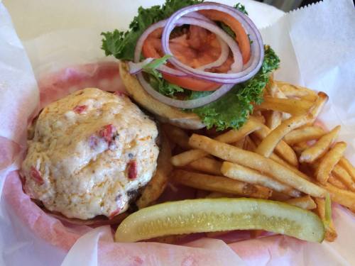 A plate featuring a burger with lettuce, tomato, and onion, served with fries and a pickle on the side.