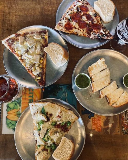 A table with four pizza slices, two breadsticks, and drinks, all on metal plates.