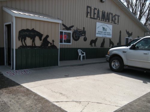 Exterior of a flea market building with animal silhouettes, a parked truck, and a white chair outside.
