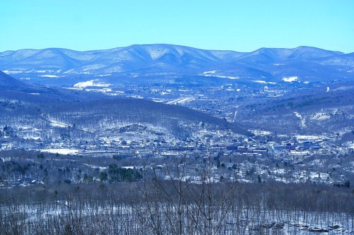 A panoramic view of snow-covered mountains and a valley, with a clear blue sky above.