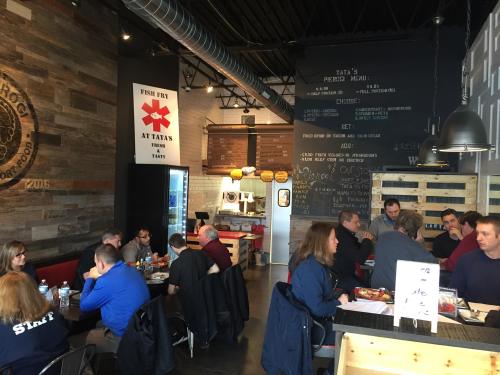 A busy restaurant interior with diners at tables, a chalkboard menu, and a modern decor featuring wood and metal elements.