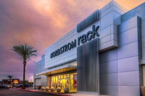 Exterior of a Nordstrom Rack store at dusk, featuring modern architecture and palm trees against a colorful sky.