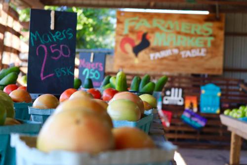 Baskets of fresh produce at a farmers market, with a sign displaying "Farmers Market" and prices.