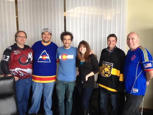 A group of six people wearing various hockey jerseys, smiling together in an office setting.
