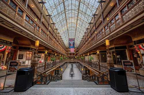 A grand indoor atrium with glass ceiling, ornate railings, and shops lining the balconies, creating a historic atmosphere.