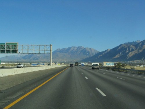 A highway stretches into the distance, flanked by mountains under a clear blue sky.