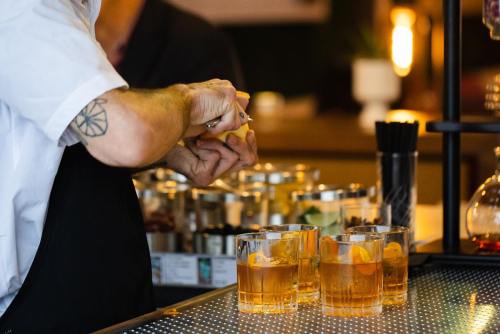 A bartender prepares cocktails with orange slices at a stylish bar, with drinks displayed in front.