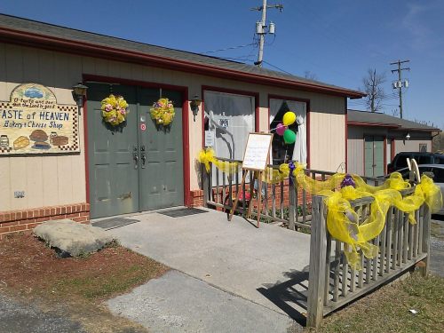 A quaint cheese shop with a decorated entrance, featuring yellow ribbons and balloons on a sunny day.