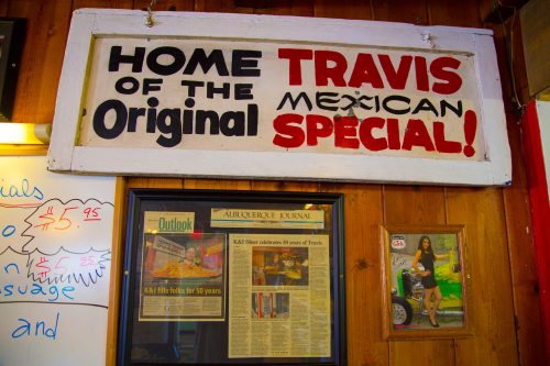 Sign reading "Home of the Original Travis Mexican Special!" with framed articles and a photo on a wooden wall.