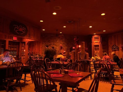 Cozy restaurant interior with wooden decor, dim lighting, and patrons dining at tables.