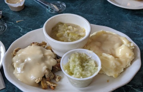 A plate with stuffing topped with gravy, mashed potatoes, and a side of green bean casserole.