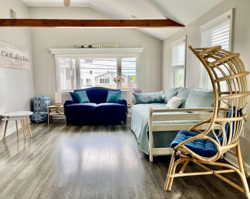 Bright living room with a blue couch, light blue accents, a rattan chair, and large windows letting in natural light.