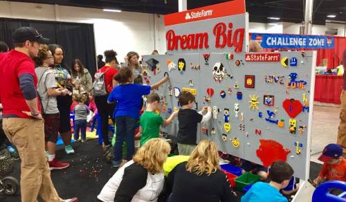Children and adults engage with a colorful activity wall at a State Farm event, creating art and enjoying the challenge zone.