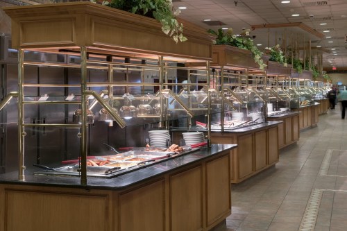 A spacious buffet with multiple food stations, featuring warm dishes under glass covers and plates ready for serving.