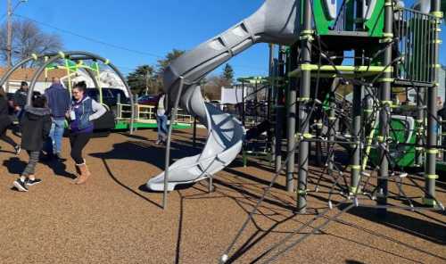 Children play on a colorful playground with a slide and climbing structures under a clear blue sky.