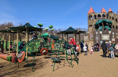 A vibrant playground with climbing structures, slides, and children playing under a clear blue sky.