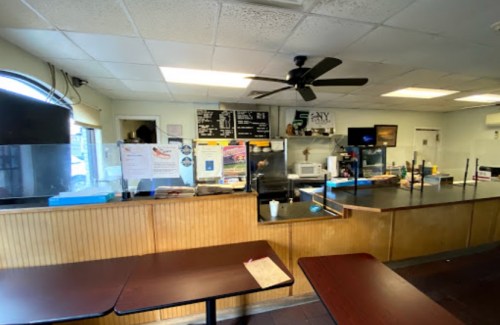 Interior of a casual eatery with a counter, menu board, and tables, featuring a fan and bright lighting.