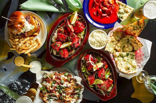 A vibrant spread of various dishes including grilled meats, naan, fries, and sauces, with drinks on the side.