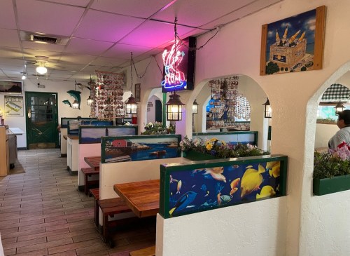 Interior of a colorful restaurant with wooden booths, fish-themed decor, and a neon sign. Bright and inviting atmosphere.