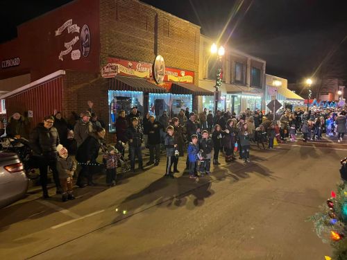 A festive night scene with a crowd of people, including children, gathered along a street decorated for the holidays.