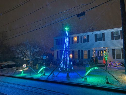 A house decorated with colorful Christmas lights, including a blue star and snow falling at night.