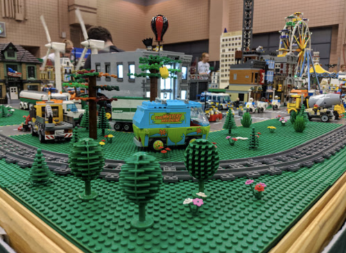 A colorful LEGO city scene with vehicles, buildings, trees, and a train track, showcasing a vibrant miniature landscape.