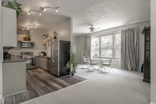 Modern kitchen with stainless steel appliances, open layout, and a dining area featuring large windows and light decor.