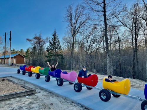 A colorful train made of large, round cars on a path, with people smiling and enjoying a fun outdoor activity.